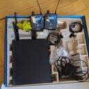V modré krabici s pěnovou vložkou je sada bezdrátového systému značky SENNHEISER. Sada obsahuje černý přijímač, dva vysílače s anténami a logo SENNHE…