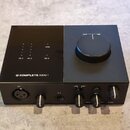 Černý zvukový interface s nápisem KOMPLETE AUDIO 1 a logem výrobce. Na horní straně jsou kontrolky s popisky IN 1, IN 2, USB a 48 V, vpravo je velký…