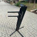 Černý kovový stojan na klávesové nástroje s dvěma vodorovnými rameny. Na hlavní nosné tyči je bílý nápis ULTIMATE SUPPORT™. Stojan stojí na dlážkovém…