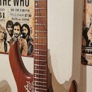 Elektrická kytara s hnědým dřevěným povrchem a hnedým hmatníkem. Na těle je viditelné logo "Ibanez". Kytara má dva snímače (jeden jednoduchý, jeden d…