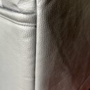 Detailní záběr na švýv a povrch šedého materiálu s texturou kůže. Na povrchu jsou vidět drobné vrásky a v místě švu je malá tmavší skvrna či oděrka.…