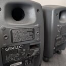 Dva šedé studiové monitory s matným povrchem. Na zadní straně levého monitoru je vidět logo GENELEC a ovládací prvky s nápisy ALL OFF, BASS TILT, DES…