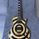 Elektrická kytara s jednovýstupním korpusem v bílo-černém pruhovaném designu. Na hlavě je logo Epiphone a vložka s ornamentem, na snímačích je nápis…