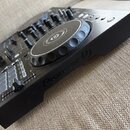 Černý DJ controller s dvěma jogovými koly a ovládacími prvky. Na boku je vyražen nápis Pioneer Dj, v centru jogového kola je logo značky. Povrch přís…