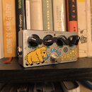 Stříbrný efektový pedál s kovovým povrchem. Na horní straně je nápis Z.VEX EFFECTS VEXTER SERIES a čtyři černé ovládací knoflíky. Na přední straně je…