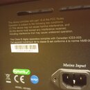 Detail zadní strany černého elektronického zařízení s napájecím vstupem označeným nápisem Mains Input. Na povrchu je text o shodě s pravidly FCC a ka…