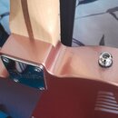 Detail zadní strany kytary v kovové barvě s hnedým javorovým hřidlem. Na kovovém krytu v místě spoje krku a těla je vyryto logo Fender. V pravé části…