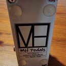 Bílá kytarový efekt pedál z kovového šasi. Na boku je černý hranatý nápis MH Pedals a pod ním text Hand Made In CZECH REPUBLIC True Bypass Pedal. V h…