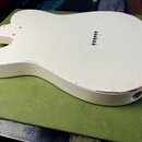 Kremově bílé tělo elektrické kytary s kovovými strunovníky. Povrch vykazuje drobné škrábance a oděrky, zejména v dolní části zadní strany. Na těle ne…