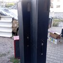 Dvě vysoké, černé sloupové reproboxy s texturovaným povrchem. Každý box má v horní části mřížku reproduktoru a na boku černou plastovou rukojeť. V po…