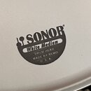 Detail bílého bubnového koženu s černým potiskem. Je na něm vidět logo SONOR, nápis White Medium a text DRUM HEAD MADE BY REMO U. S. A.. Povrch je hl…