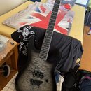 Elektrická kytara s černým povrchem a šedou strukturou dřeva na topu. Nástroj má dva humbuckery, jeden ovládací knoflík a hmatník s bílými značkami.…