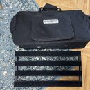 Černý přepravní kufr z textilie s rukojetí a předním kapsáčem, na kterém je bílý nápis ROCKBOARD by WARWICK. Před kufrnem leží černá pedalboard zákla…