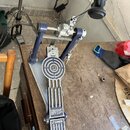 Modrý a stříbrný basový pedál s kovovou základnou. Na šlapce jsou nápisy GIANT STEP a SONOR. Povrch pedálu vykazuje známky používání v podobě drobnýc…