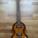 Čtyřstrunná basová kytara s tělem ve tvaru houslí a barevným přechodem od žluté k tmavě hnědé. Na hlavě je viditelné logo Epiphone. Nástroj má dva sn…