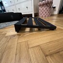 Černý podložkový stojan s několika paralelními vložkami z tmavého, texturovaného materiálu. Předmět je umístěn na dřevěné podlaze v interiéru. Na sto…