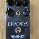 Černý kytarový efekt s nápisem DRACARYS DISTORTION a logem WAMPLER BUILT IN USA. Na horní straně jsou čtyři černé otočné knoflíky s popisky VOLUME, M…