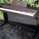 Digitální piano v tmavě hnědé dřevěné provedení s černým spodním panelem. Na horním stojáku na noty je bílý nápis CELVIANO a vpravo nad klávesami je…