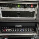 Fotografie zachycuje dva přístroje v transportním racku. Horní zařízení je černé s nápisy the t.racks a VM-100, má několik ovládacích prvků a svítící…