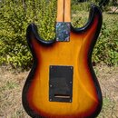 Zadní strana elektrické kytary s tělem v provedení sunburst (žluto-černý přechod). Na kytaru jsou připevněny dvě černé krytky, z nichž horní nese neč…
