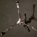 Kromě černého podkladu je na fotografii vidět chromovaný bubnový pedál s třemi černými gumovými nášlapníky. Nástroj je z kovového materiálu s lesklým…