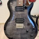 Elektrická kytara s tmavě šedým lakem a viditelnou strukturou dřeva na topu. Nástroj má dva humbuckery s černými kryty, čtyři otočné knofíky a přepín…