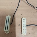 Dvě elektrické snímače v krémovém provedení s plastovými kryty. Levý snímač je typu humbucker s nápisem "Seymour Duncan". Pravý snímač je typu single…