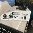 Bílý přístroj s ovládacími prvky a displejem, umístěný v originální krabici. Na zadní straně jsou konektory s popisky GTR / AMP IN, SPEAKER OUT, USB…