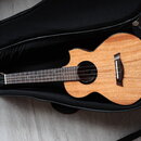Dřevěné ukulele s přirozenou barvou a vyřezem v deskách leží v černém polstrováním pouzdře. Na hmatníku jsou vidět bílé polohové značky ve tvaru ovál…