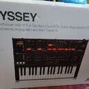 Fotografie zachycuje kartonovou krabici s obrázkem analogového syntetizátoru. Na krabici je velký nápis ODYSSEY a text Analog Synthesizer with 37 Ful…