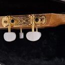 Detail zadní strany hlavy akustického nástroje z přírodního dřeva. Jsou vidět tři zlaté ladičky s bílými plastovými knoflíky a ozdobným kovovým kryte…