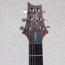 Fotografie zachycuje hlavu a horní část hmatníku elektrické kytary z tmavého dřeva. Na hlavě je bílý nápis „Paul Reed Smith“ a na černém plastovém kr…