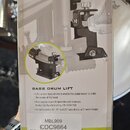 Fotografie znázorňuje kartónové balení příslušenství s nápisem BASS DRUM LIFT. Na obalu je zobrazen černý kovový mechanismus s pružinou a v dolní čás…