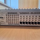 Zadní strana stříbrného mixážního pultu s nápisem BEHRINGER EURORACK MX 2642A. Jsou zde vidět různé vstupy a výstupy, včetně osmi kombinovaných konek…