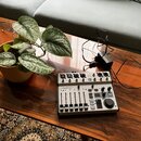 Na dřevěném stole je umístěn kompaktní mixážní pult stříbrné barvy s černými ovládacími prvky. Na zařízení je viditelné logo Behringer a nápis FLOW 8…