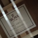 Fotografie zachycuje vnitřní štítek akustické kytary. Na bílém štítku je logo SIGMA s nápisem EST.1970, označení Model GMC-1E a Serial No. 241203957.…