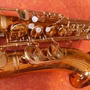 Zlatý saxofon s kovovým povrchem a bílými polštářky na klapkách. Na těle nástroje jsou viditelné gravírované ornamenty a nápisy, které nejsou z tohot…
