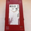 Červený kovový box s bílou nálepkou na horní straně. Na nálepce jsou viditelné symboly pro recyklaci, nápis RoHS a texty: „Conforms to ICES-003“, „Co…