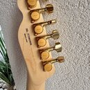 Záběr na hlavu světle hnědé dřevěné kytary s šesti zlatými ladičkami. Na každém ladičku je vyryté logo GOTOH. Na zadní straně hlavy je nápis SERIAL N…