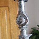 Detail chromovaného stojanu s černým pěnovým tlumicím prstencem v horní části. Na kovovém kloubu je vyryté nečitelné označení. Povrch chromu vykazuje…