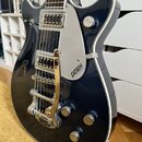 Tmavě modrá elektrická kytara s bílým lemováním a chromovanými prvky. Na stříbrném plechu je nápis GRETSCH ELECTRONIC a na mechanismu tremola značka…