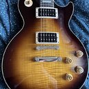 Elektrická kytara s trupem v barvě sunburst a viditelnou strukturou dřeva. Nástroj má dva humbuckery s bílými rámečky, čtyři zlaté ovládací knofíky a…
