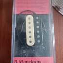 Fotografie znázorňuje kytarový snímač typu humbucker v originálním plastovém obalu s červeným papírem. Snímač má bílé plastové krytí s viditelnými pó…