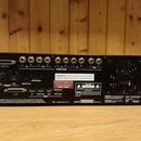 Zadní strana černého rackového hudebního modulu. Na panelu jsou vidět různé konektory, včetně řady jackových výstupů s nápisem Audio Outs a portů SCS…