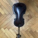 Tmavně hnědá smyčcová nástroj, pravděpodobně viola nebo housle, položená na dřevěné parketové podlaze. Nástroj má lakovaný povrch s viditným odleskem…