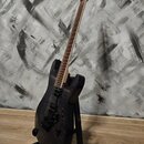Elektrická kytara s tmavým, pravděpodobně prožilkovaným povrchem těla a hmatníkem. Nástroj má dva humbuckery, černý most s páčkou a světlý krk. Na hl…