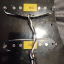Fotografie zachycuje dvě černé elektrické snímače s viditelnými bílými a černými vodiči, které jsou umístěny na černém povrchu. Horní snímač má žlutý…