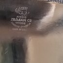Detail kovového činely s jemným žilkováním povrchu. Uprostřed je vyražen nápis: AVEDIS ZILDJIAN Co GENUINE TURKISH CYMBALS MADE IN USA. Nad textem je…