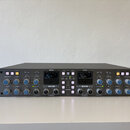 Šedý rackový studiový kompresor s nápisy Solid State Logic vlevo a THE BUS+ vpravo. Přední panel obsahuje dva analogové VU metry, řadu regulačních kn…