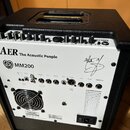 Zadní strana bílého komba s černým krytem. Na bílém panelu jsou nápisy AER The Acoustic People a MM200 spolu s logem ve tvaru srdce. Jsou zde vidět r…